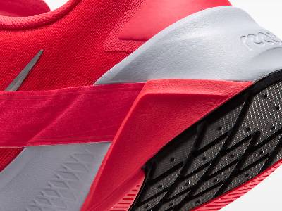 Детайлен изглед отблизо на задната част и петата на червена маратонка Nike Hybrid RN, показващ сивата междинна подметка с лого React, червения страничен омекотяващ елемент и грапавия грайфер на подметката. 