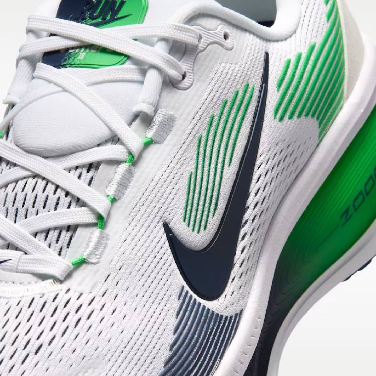 Близък план на горната част на бели мъжки маратонки Nike Vomero 18 със зелени акценти, бели връзки и тъмносиньо лого на Nike